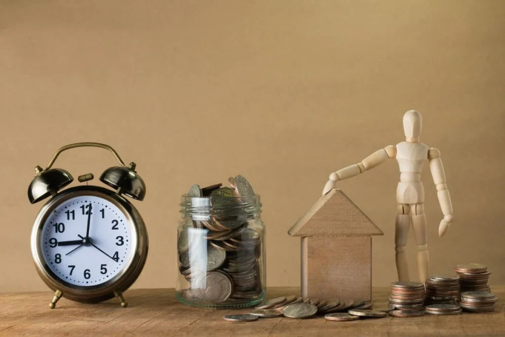 Figura de madera junto a una casa, monedas y un reloj
